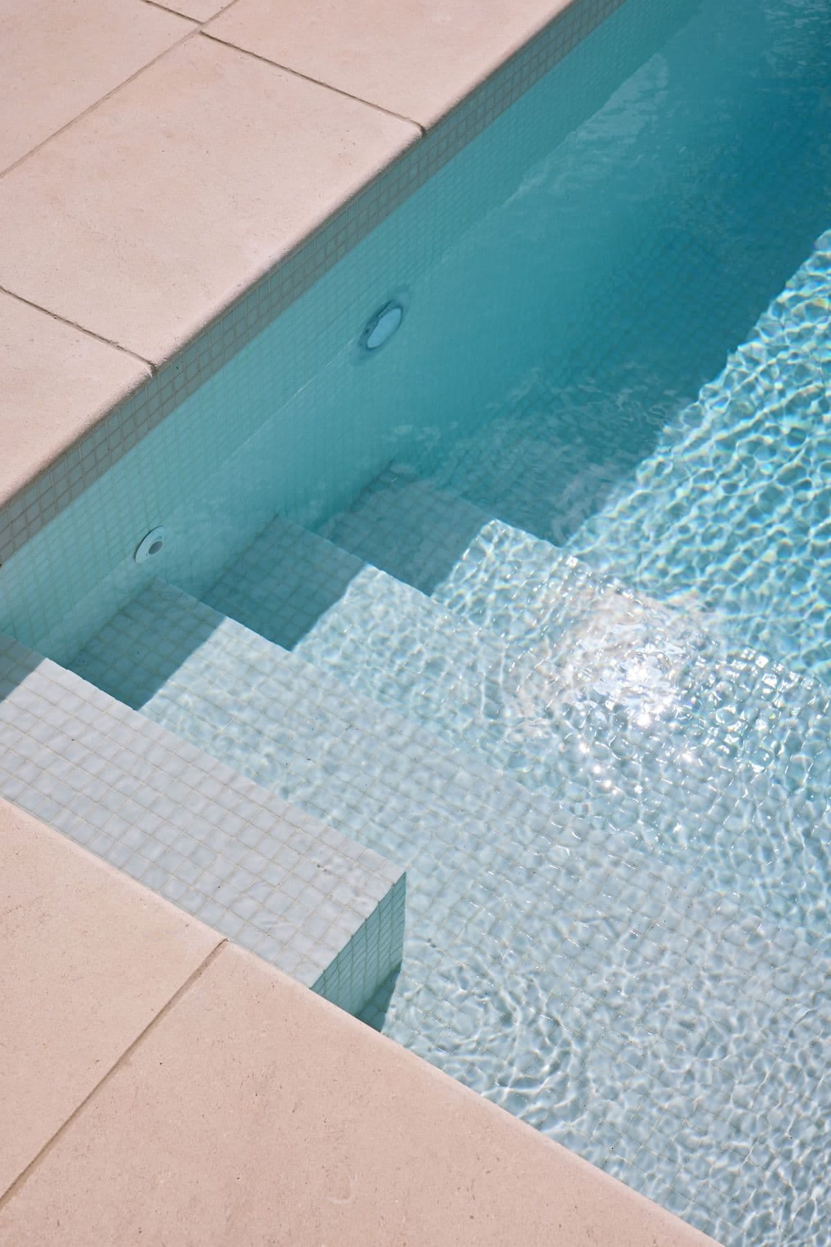 Submerged entry steps and the spa edge, sunlight rippling across the pale tiled floor.