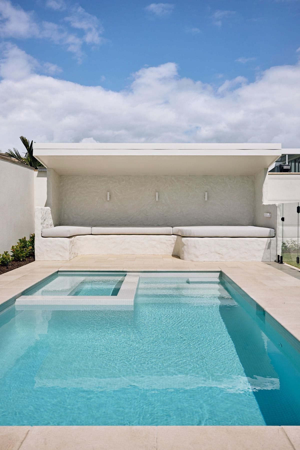 The cabana square on across the pool, its bench seat and cushions beneath a deep white eave against cloud.