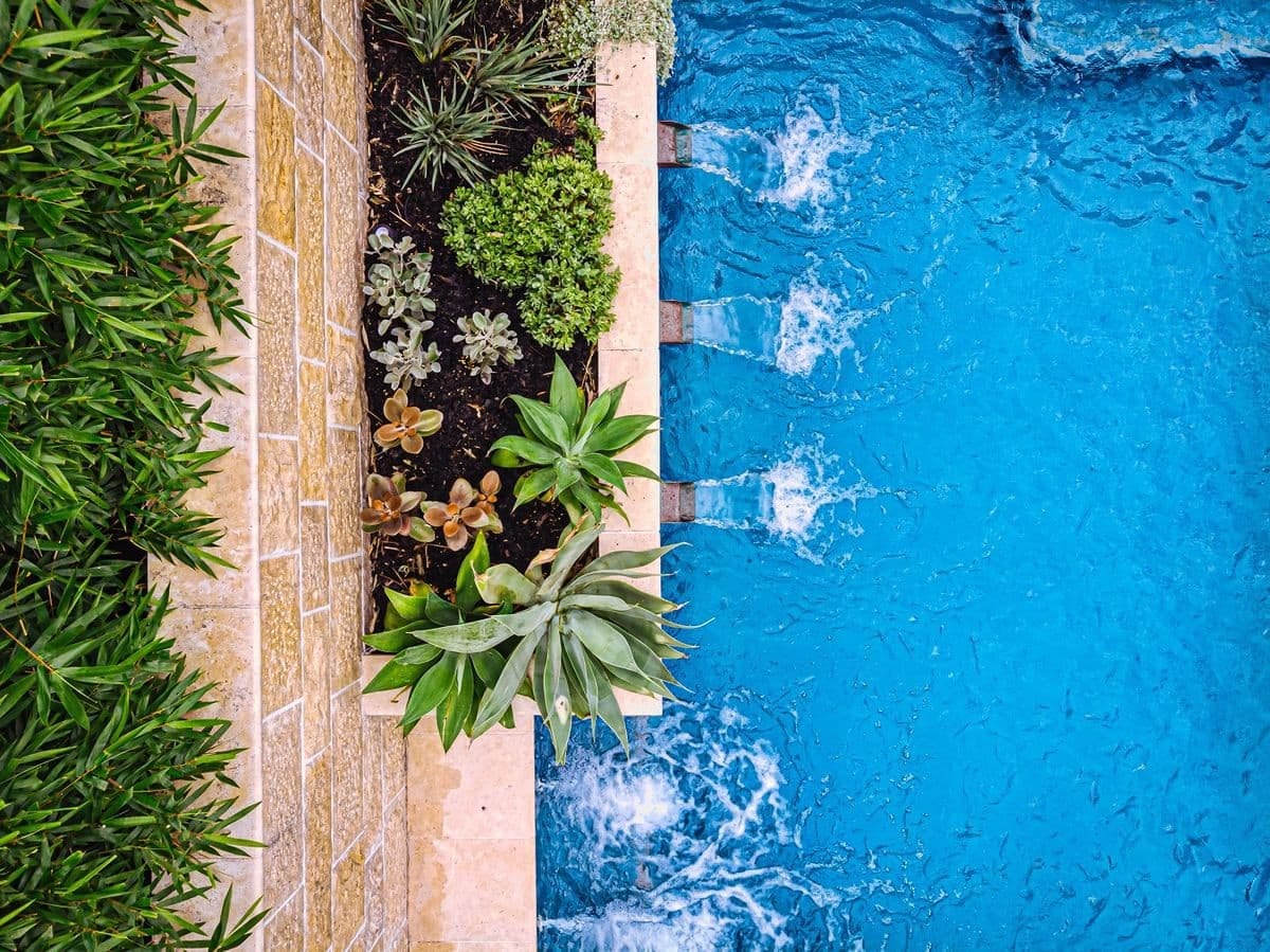 Looking straight down on the raised planter, its succulents and three water blades spilling into the blue tiled pool.