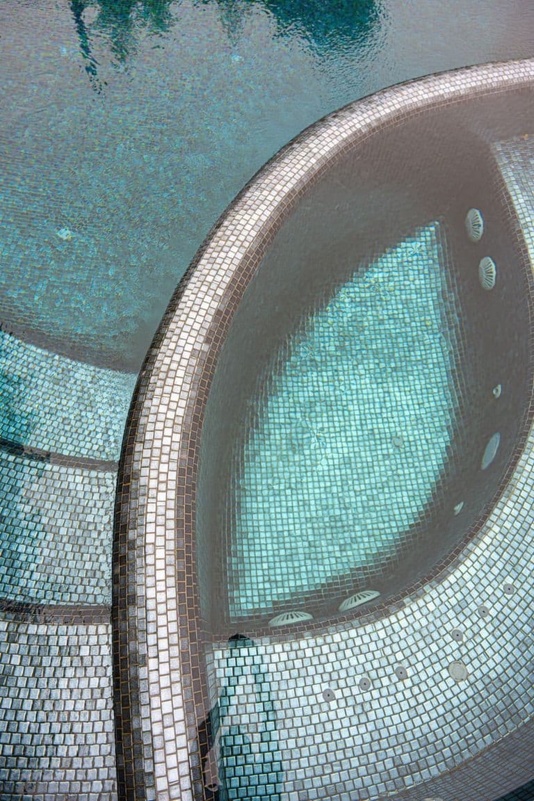 Overhead detail of the spa's curved mosaic wall meeting the pool, jets visible beneath the surface.