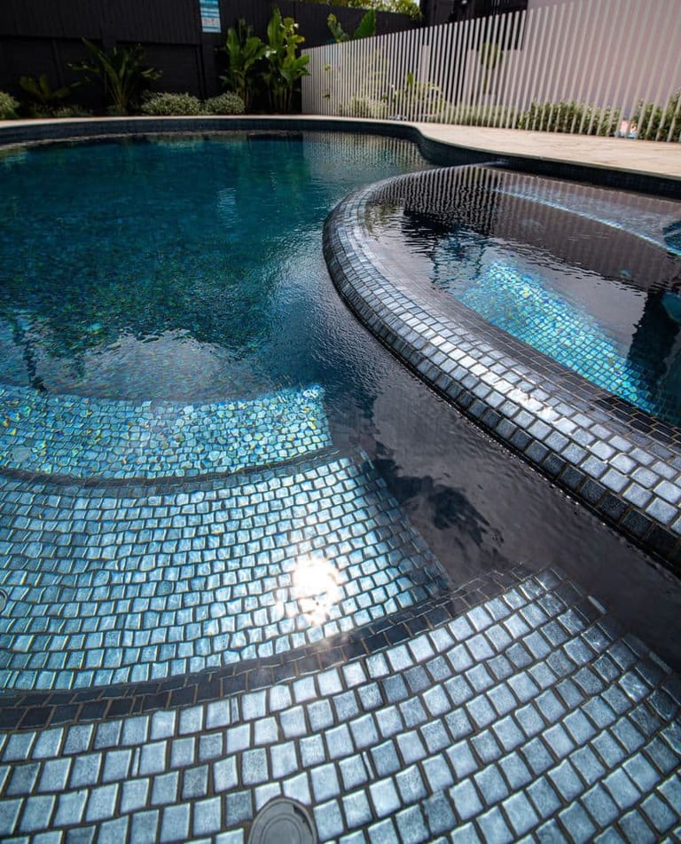 The spa's curved edge in dark mosaic against the pale shelf tiling, sunlight glancing off the water.