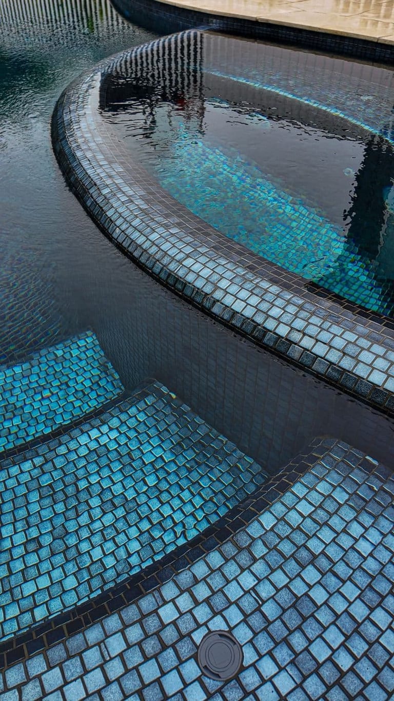 The spa's curved wall and the pool's submerged steps, mosaic shifting from blue to green.