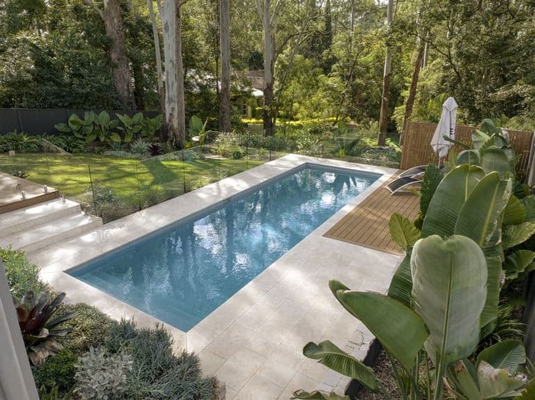 Elevated view of the lap pool, surrounding travertine and the lawn running back into leafy bushland.