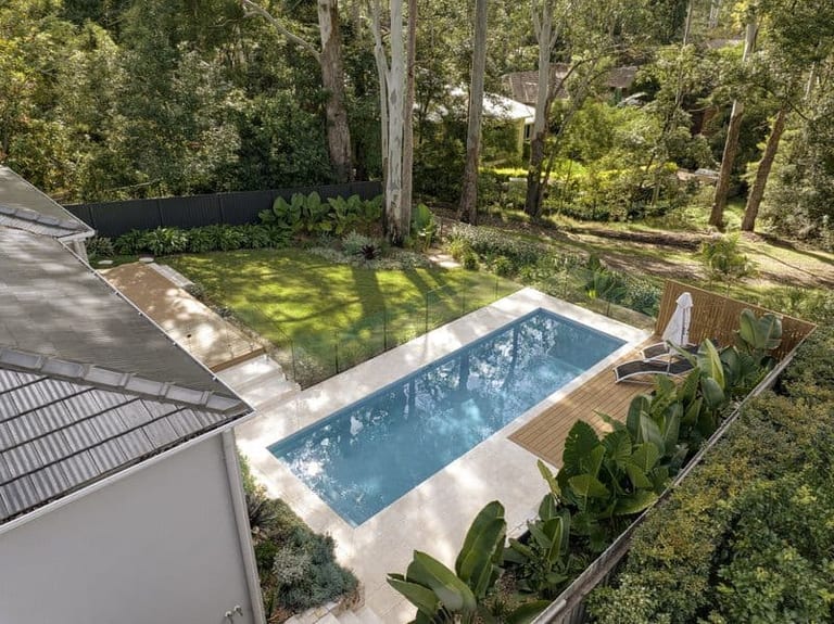 Aerial view across the house roof to the pool, lawn and tree canopy beyond.