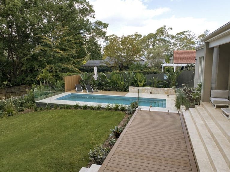 The pool, lawn and timber walkway seen from the house terrace, tropical planting along the rear fence.