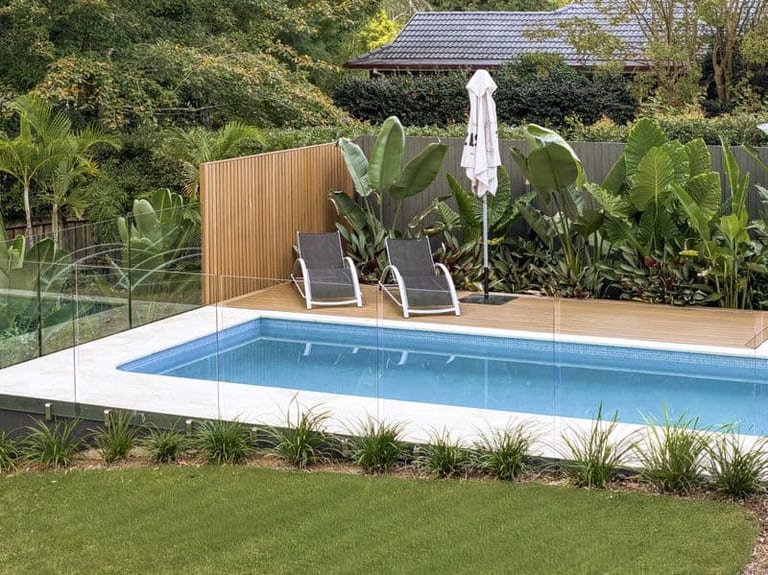 Two loungers on the timber deck behind a slatted privacy screen, with bird of paradise against the fence.