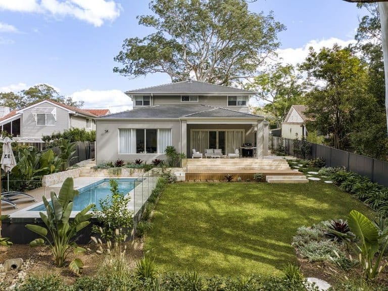 The full backyard from the rear: lawn sweeping up to the rendered house and covered terrace, pool at left.