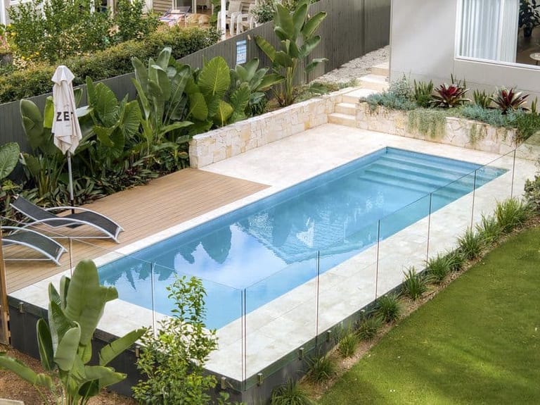 The pool from above with its submerged steps, timber deck, sandstone retaining wall and lawn at right.