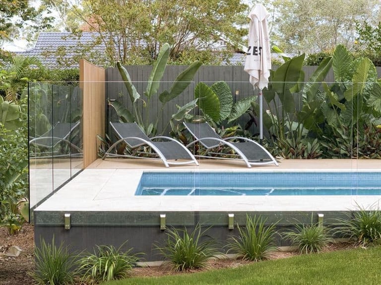 Loungers and umbrella on the timber deck beside the pool, framed by broad-leafed planting.
