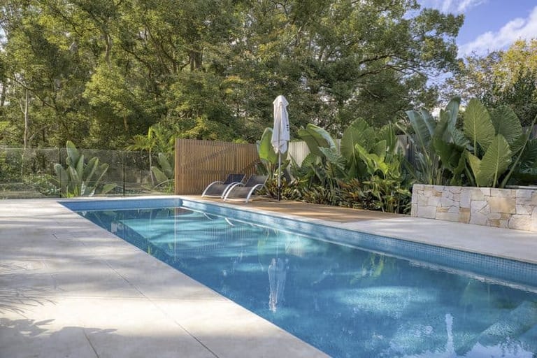 The pool at ground level with the deck, privacy screen and a sandstone planter wall catching afternoon light.
