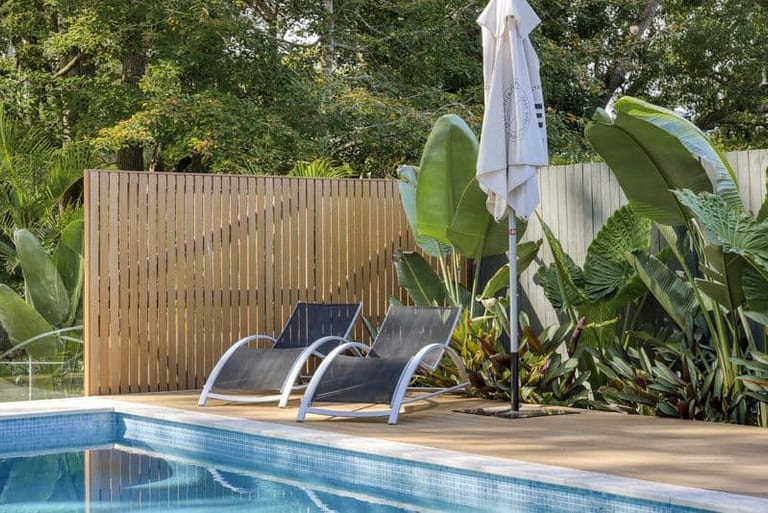 Two loungers and a folded umbrella on the timber deck in front of a slatted timber screen.
