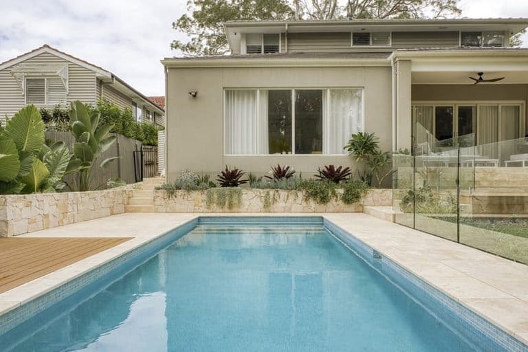 The pool looking back at the rendered two-storey house, with a sandstone planter of bromeliads along its base.