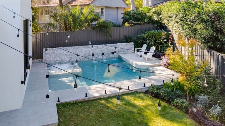 Elevated view of the pool, its raised sun shelf and the festoon lights strung above the lawn.