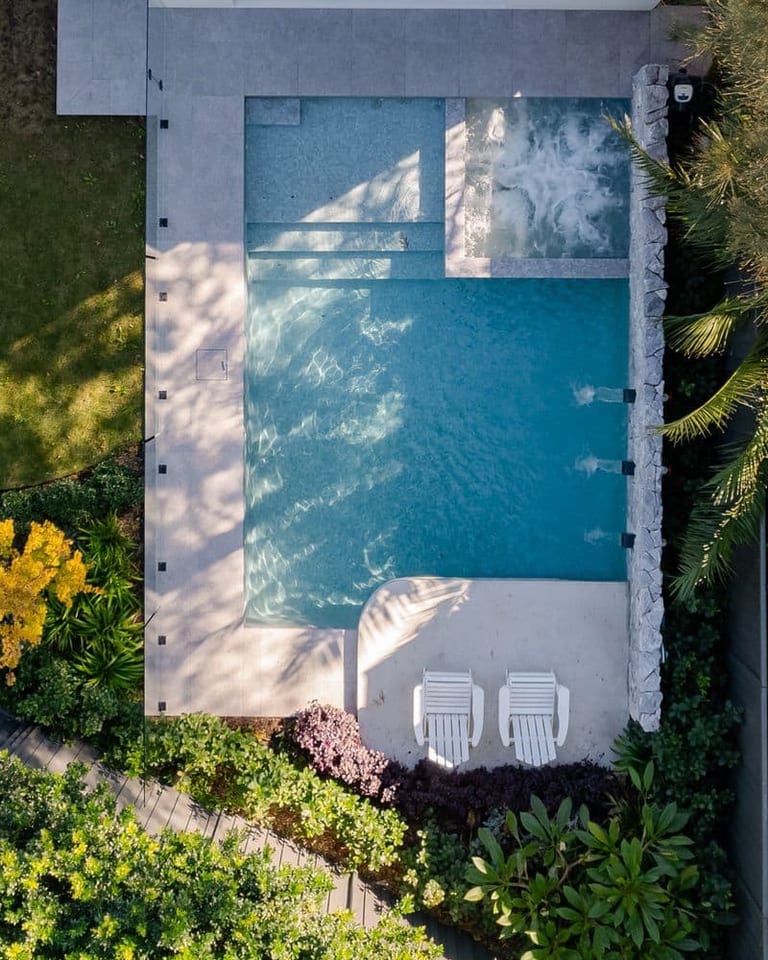 Aerial view of the pool with its sun shelf, two white chairs and surrounding planting.