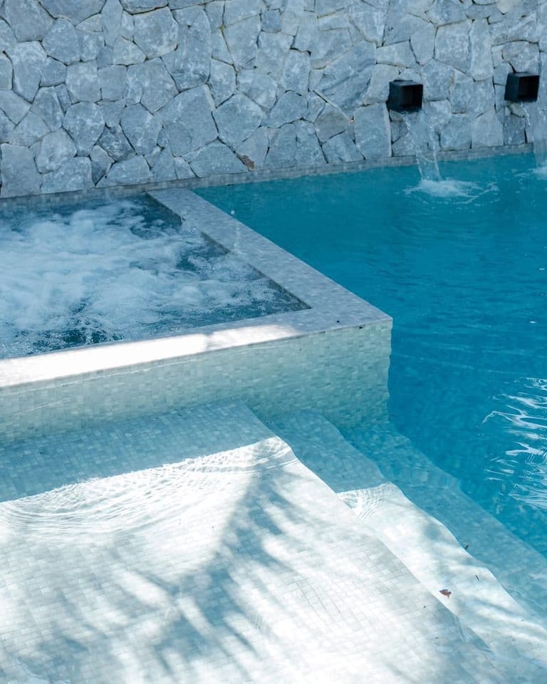 The spa corner meeting the pool, with water spouts in the stone wall and submerged steps below.