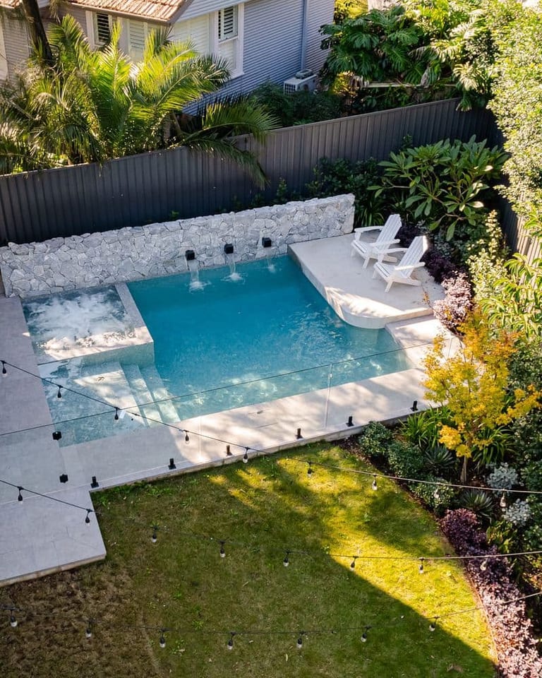 The pool from above with its stone wall, sun shelf and festoon lighting across the lawn.
