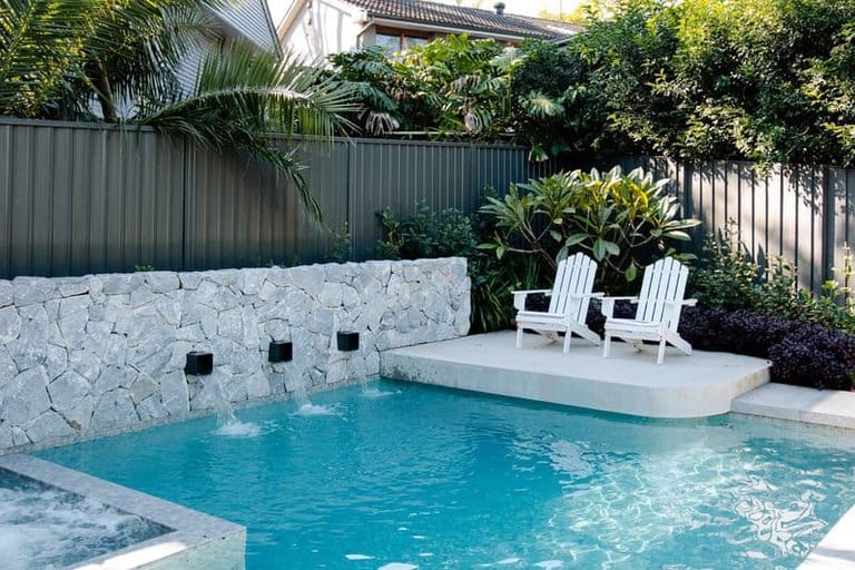 Two white Adirondack chairs on the raised sun shelf, framed by frangipani and tropical planting.
