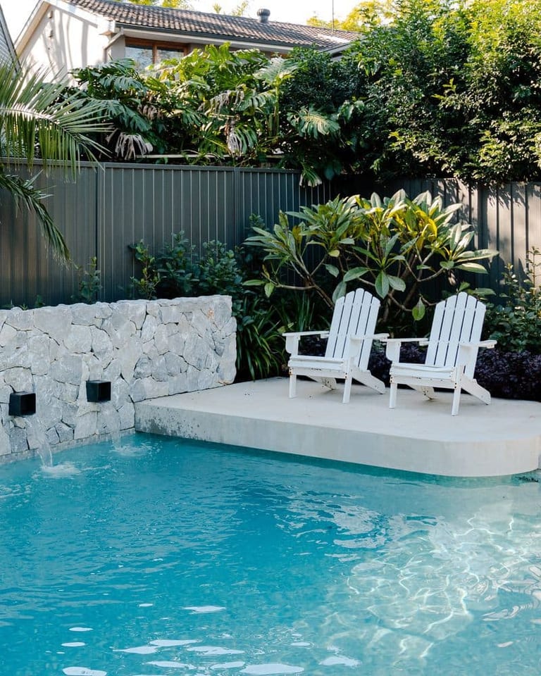 The sun shelf and chairs above the pool, with the stone wall and its spouts at left.