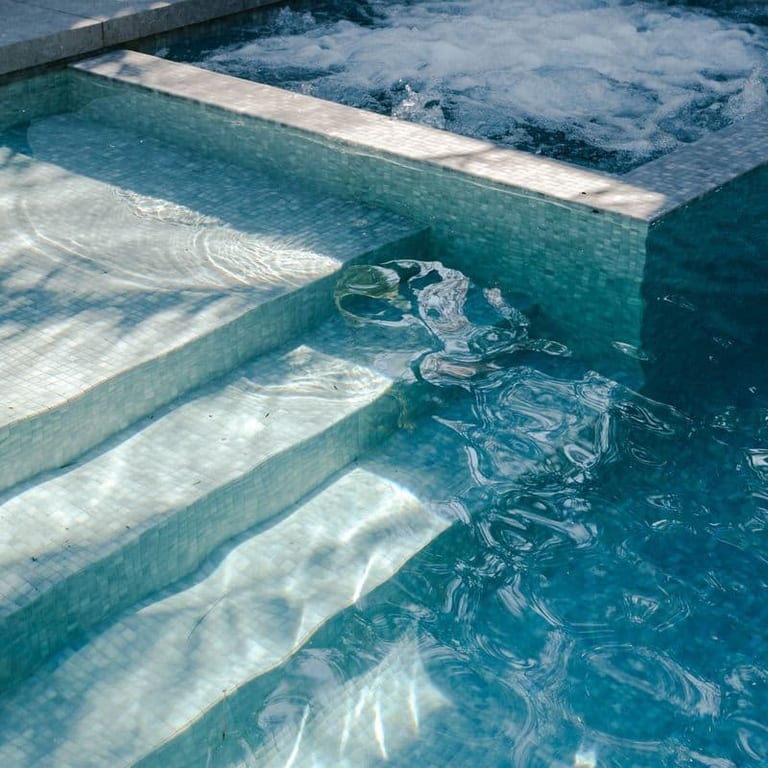 Close detail of the pool's submerged steps and the spa's bubbling surface beyond.