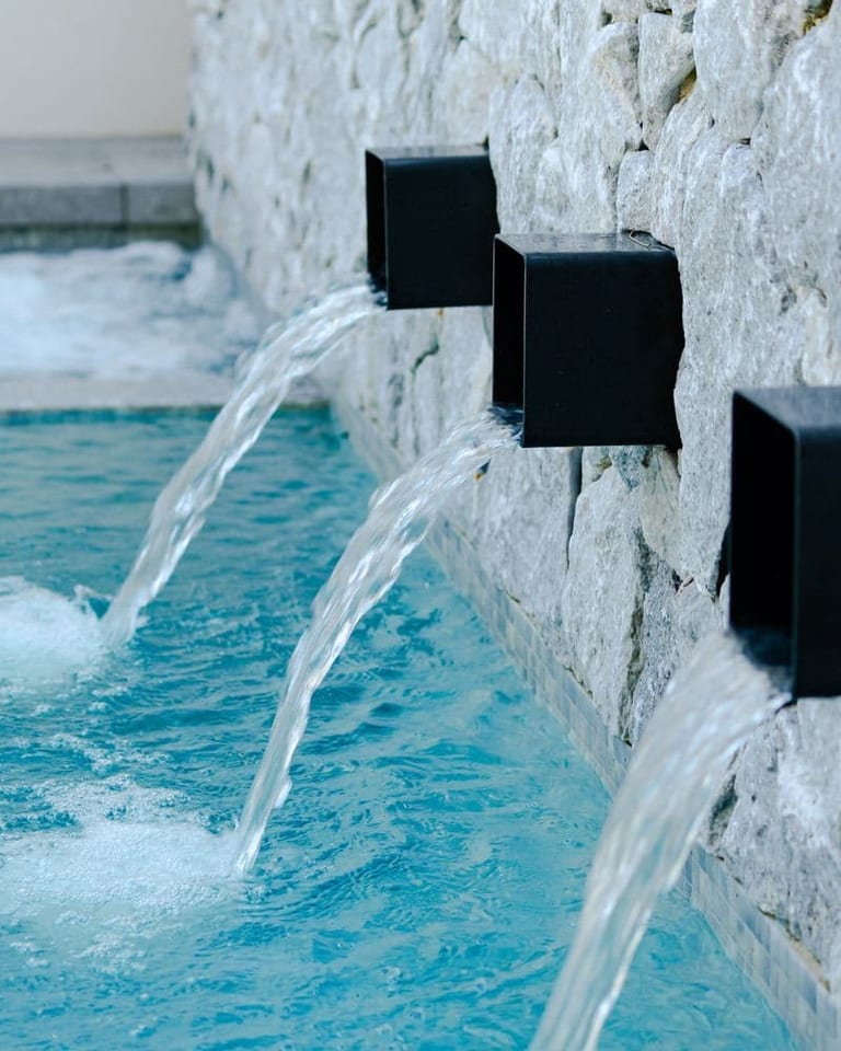 Close view of the spouts in the stone wall, water arcing into the turquoise pool.