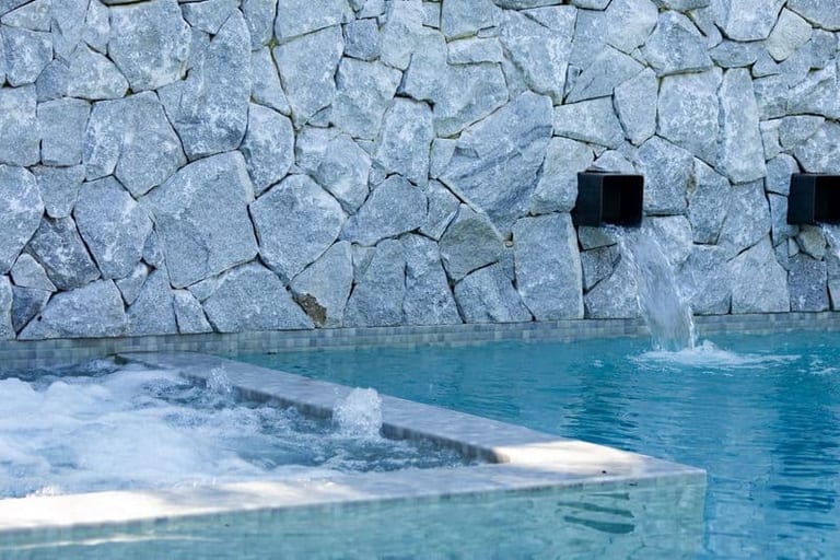 The stone wall and its spouts above the pool, with the spa bubbling at left.