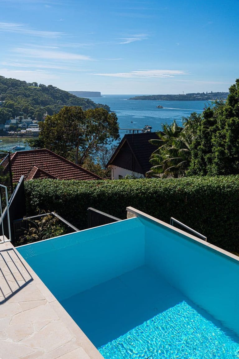 The infinity edge looking out over Sydney Harbour, with headlands and moored boats beyond the hedge.