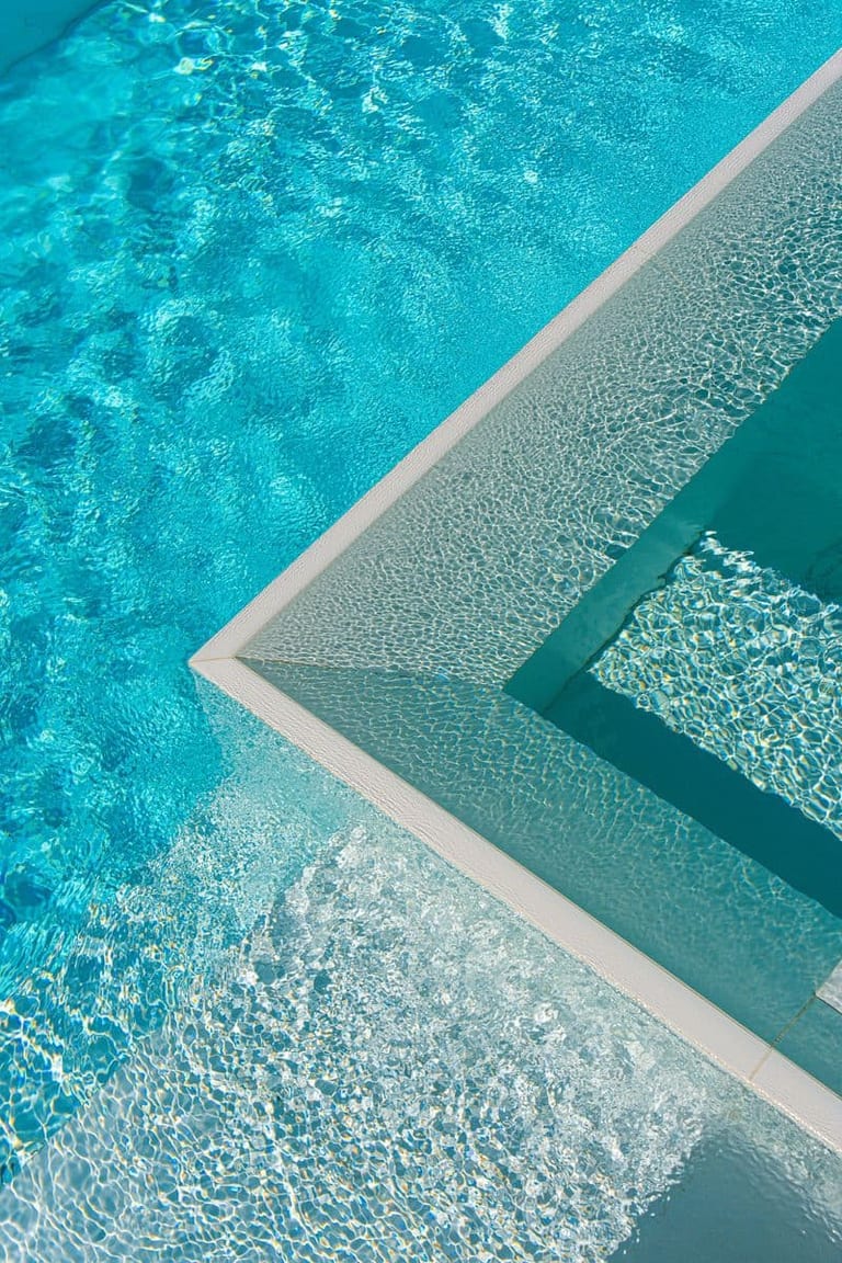 Close detail of the spa's tiled corner, the water surface broken into facets by sunlight.