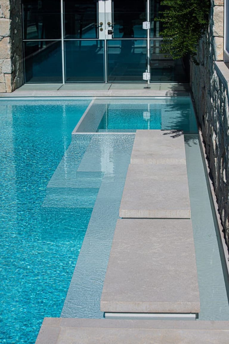 Stepping pads and submerged steps leading to the pavilion's glass doors at the shallow end.
