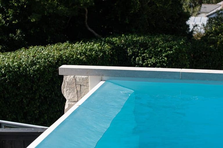 The infinity edge spilling over its stone-capped wall, a dense hedge directly behind.