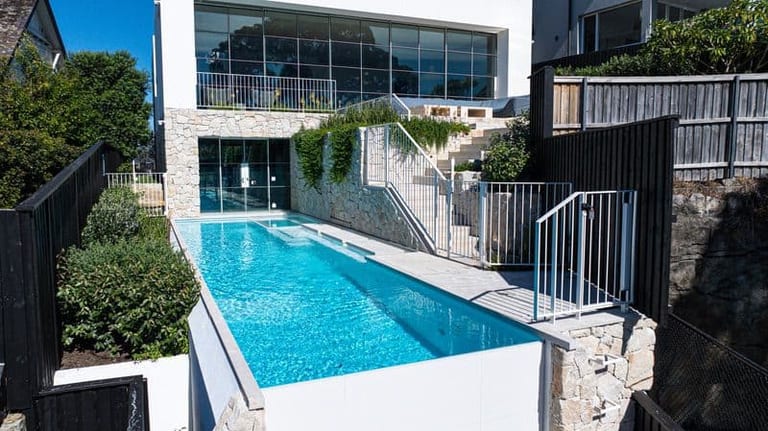 The pool seen from the garden, with the house above, stone retaining walls and balustrade stairs.