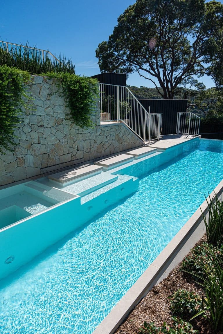 The pool, spa and stepping pads against the stone retaining wall, with trailing plants and a gum above.