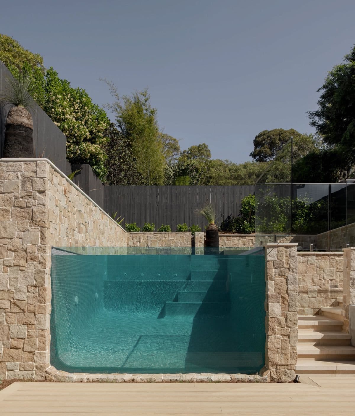 The glass viewing wall head on, submerged entry steps visible through the turquoise water between sandstone piers.