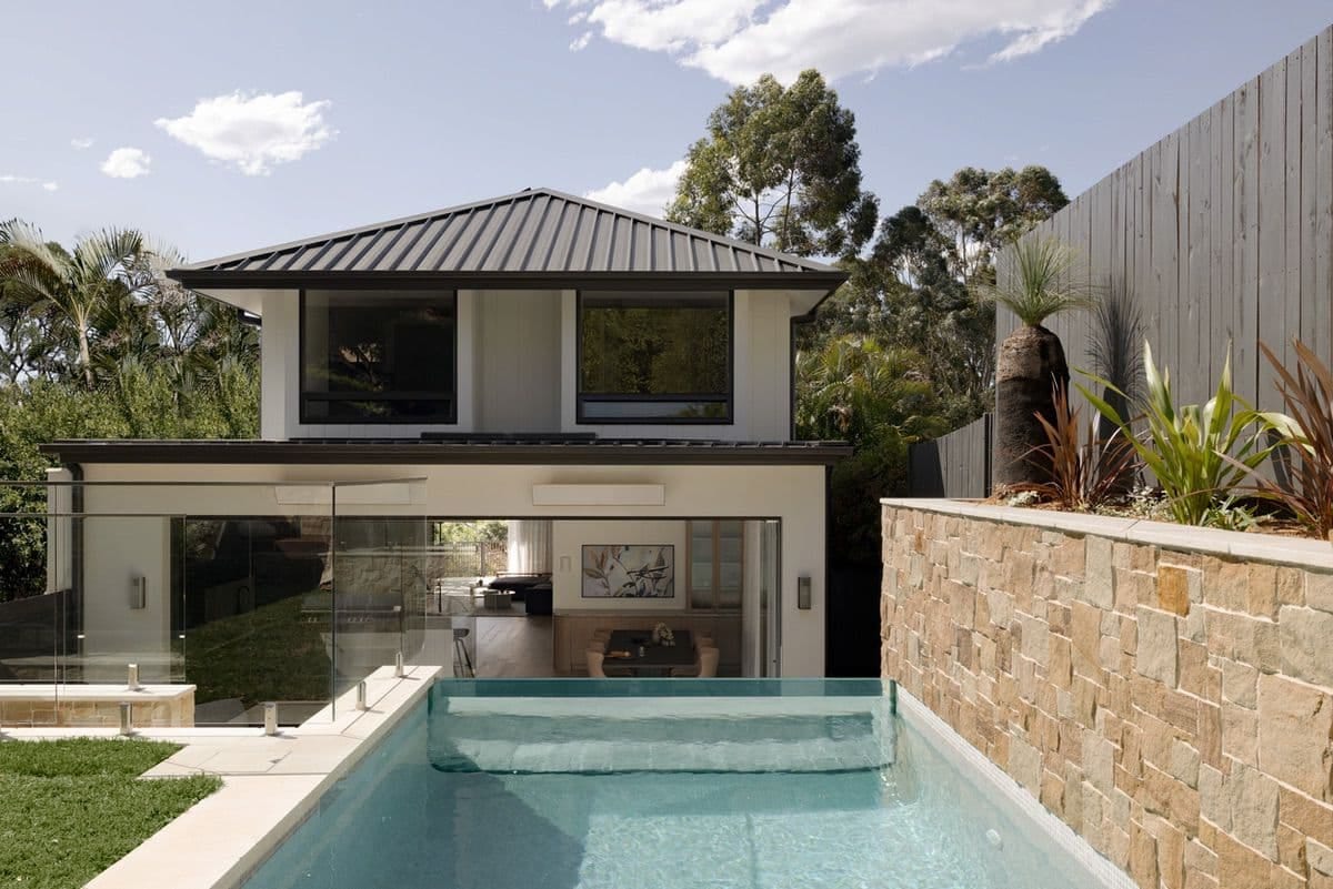 The pool in front of the house, with sliding glass doors open to the living room and a grass tree on the stone wall.