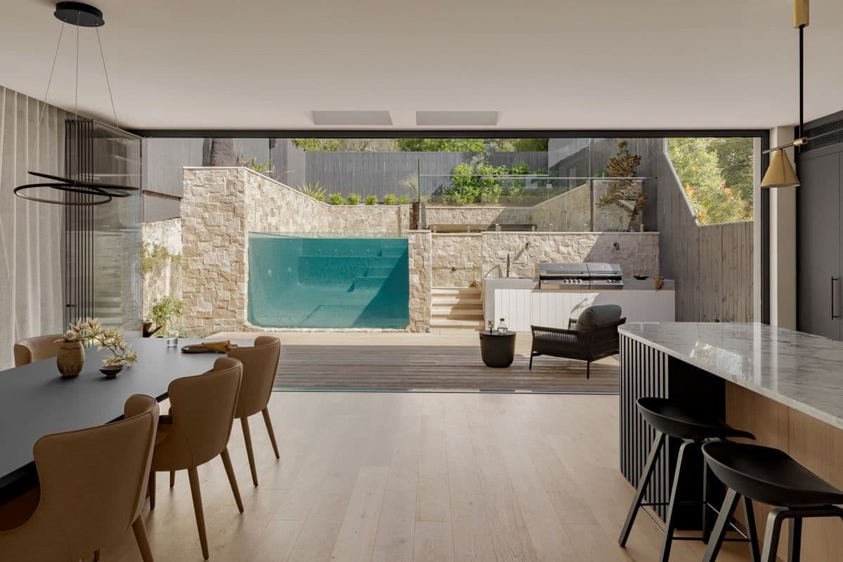 Looking out from the dining room through open sliding doors to the glass-walled pool and outdoor kitchen.
