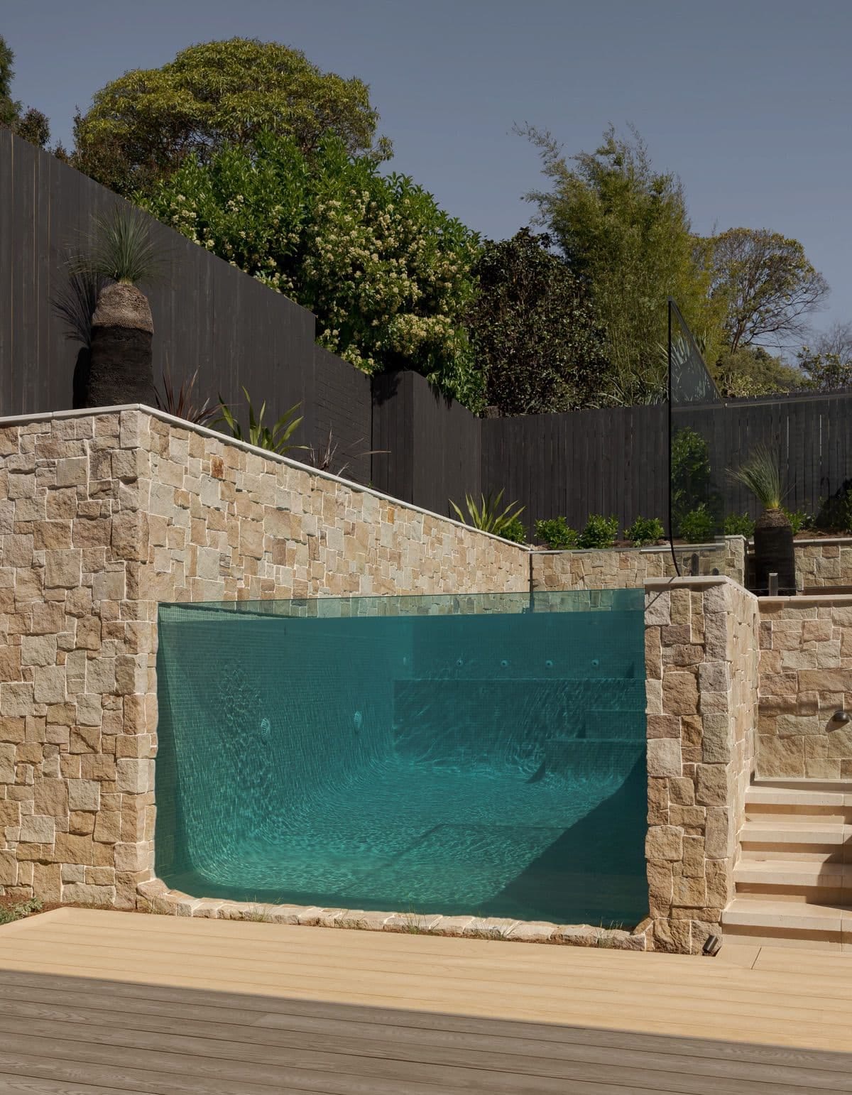 The glass viewing wall seen square on from the timber deck, sandstone steps climbing to the garden at right.