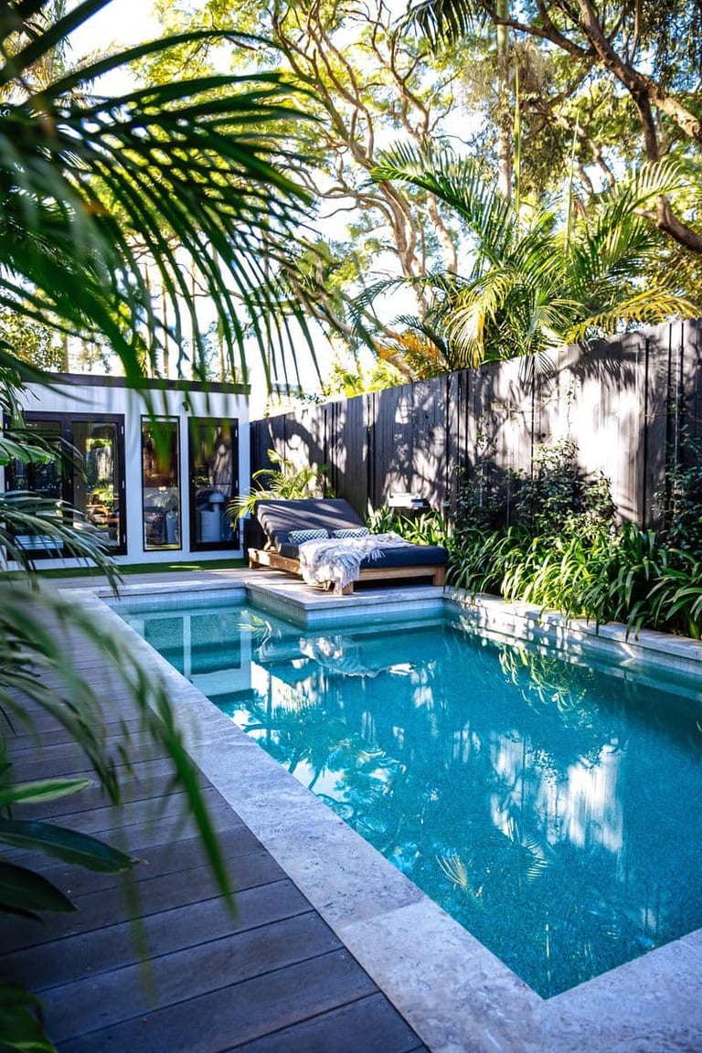 The courtyard from the deck corner, pool, daybed and studio under a canopy of palms and gums.