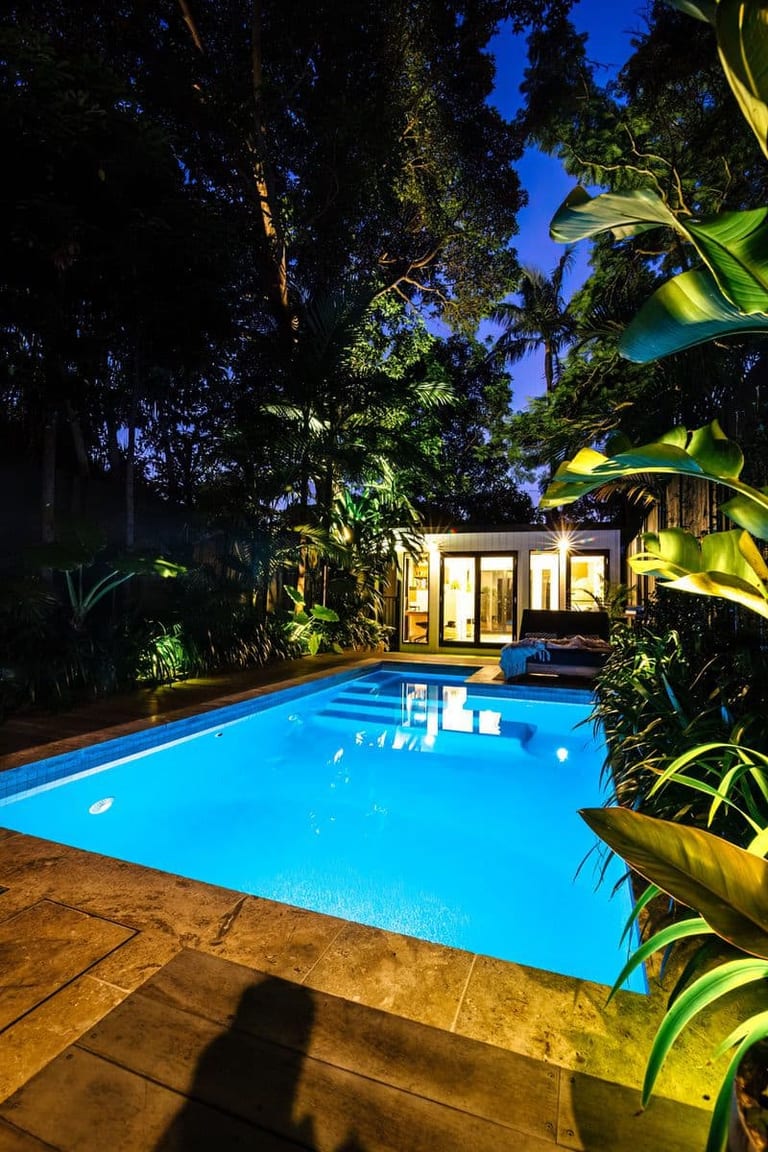 The pool lit blue at dusk, the studio glowing warm behind it under a deep blue sky.