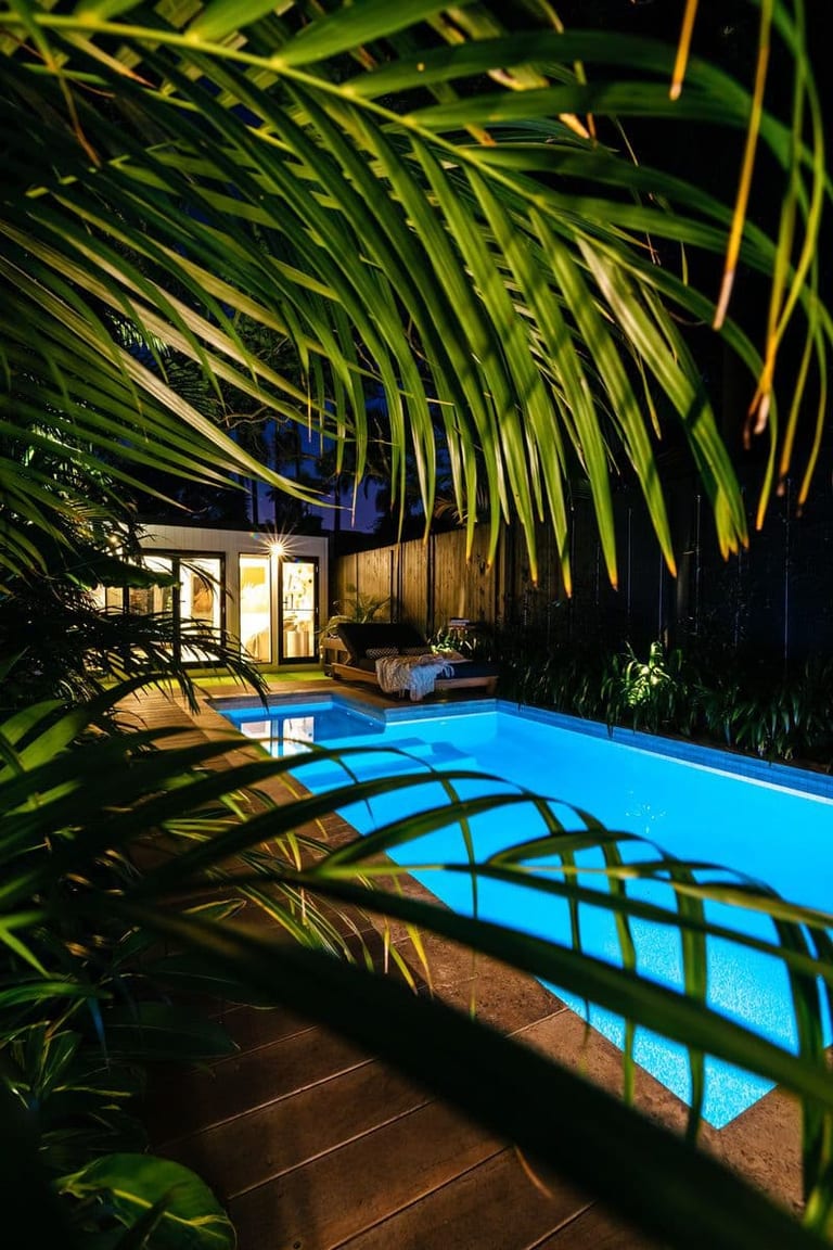 Palm fronds in the foreground at night, the lit pool and studio beyond them.