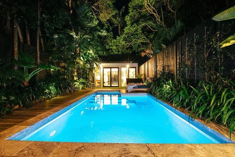 The courtyard at night seen down the pool's length, the studio lit at the far end.