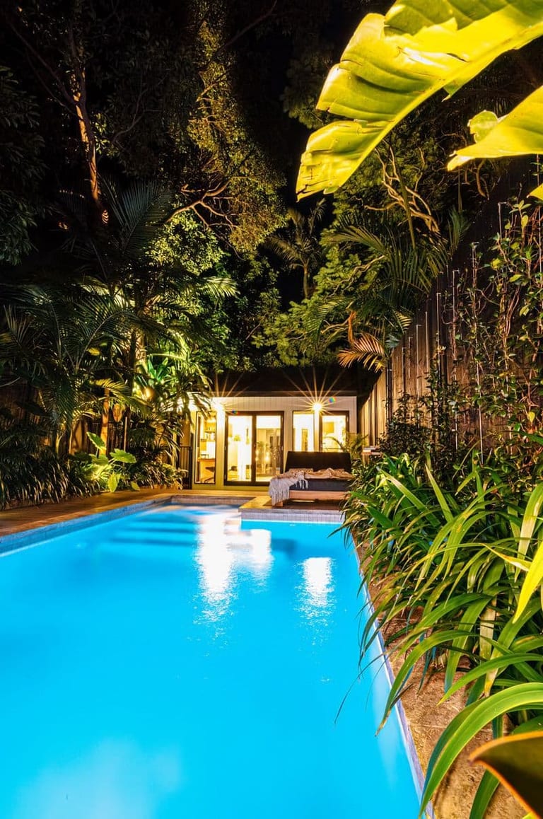 The lit pool at night with banana leaves overhead and the studio's open doors beyond.
