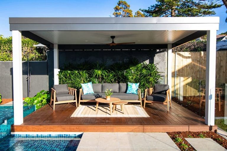 The covered pavilion with its lounge setting, rug and ceiling fan, the pool in the foreground.