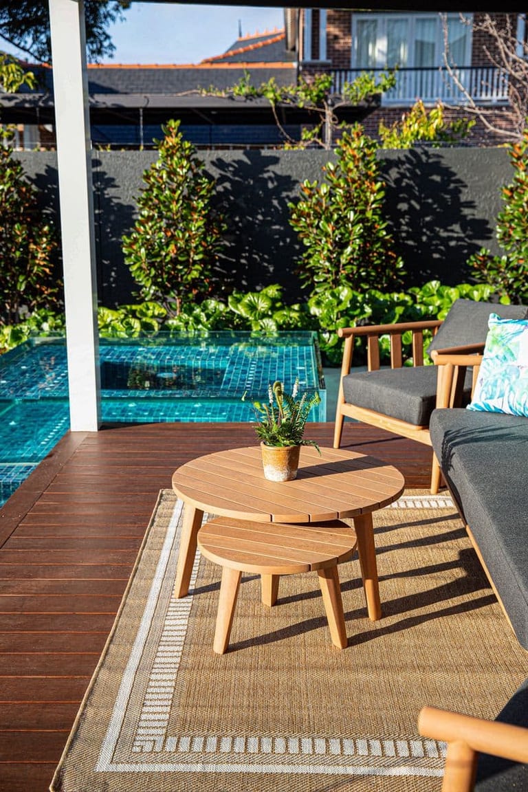 Timber side tables and lounge chairs on the deck, with the glass spa visible past the pavilion post.