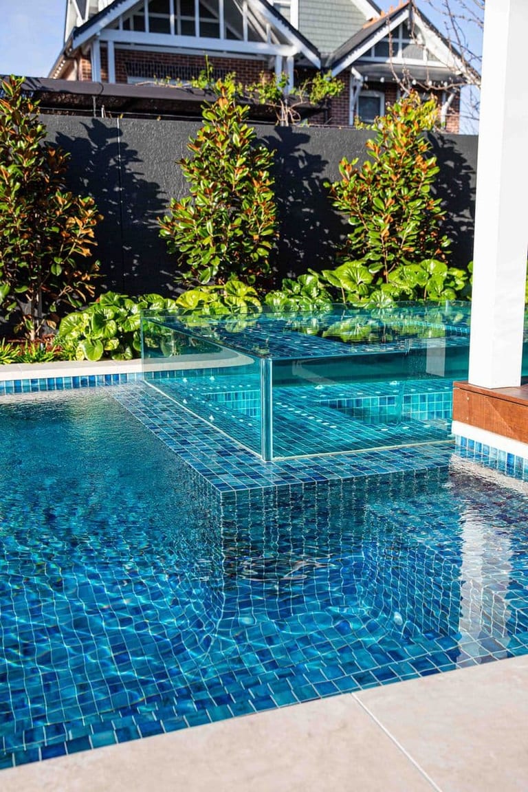 The glass-walled spa raised within the pool, magnolias and a rendered wall behind it.
