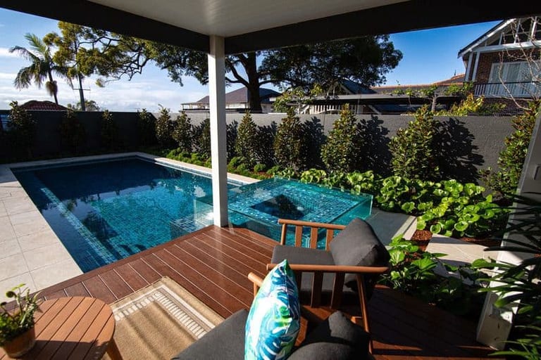 The pool and glass spa from the covered terrace, lounge cushions in the foreground.