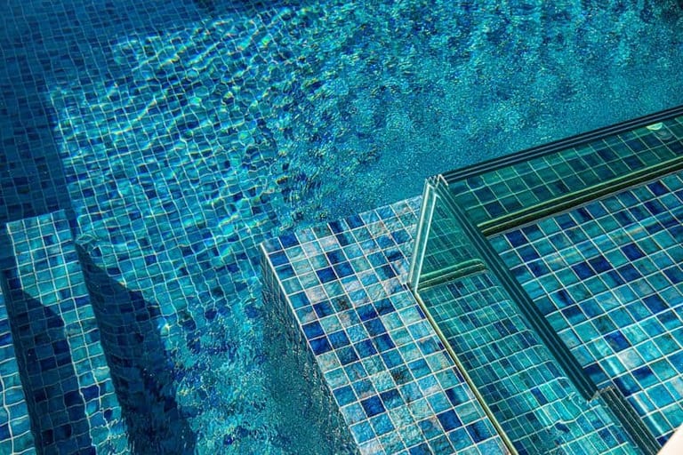 Close detail of the pool's blue mosaic steps meeting the glass spa wall.