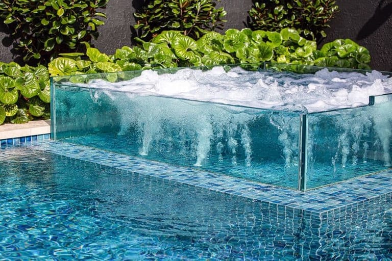 Water cascading down the glass wall of the spa as it spills into the pool below.