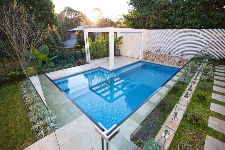 The pool at dusk from above, the white pergola catching the last light and stepping stones running up the slope.