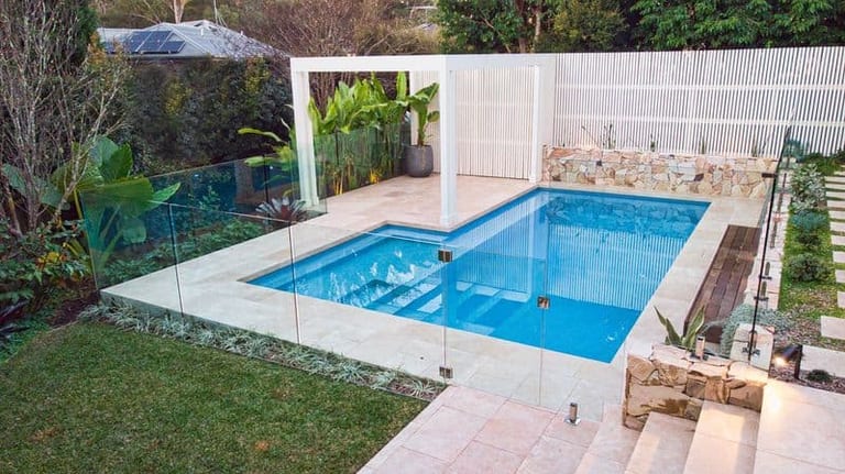 The pool, pergola and sandstone wall from the lawn, glass fencing tracing the terrace edge.