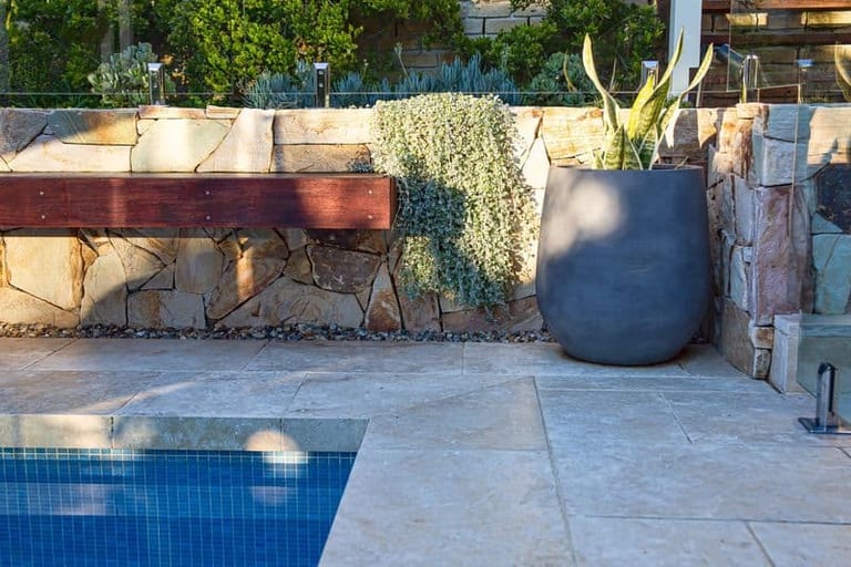 A timber bench cantilevered from the sandstone wall, with trailing silver foliage and a charcoal pot.