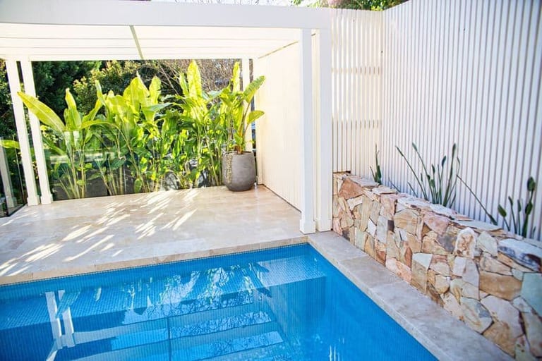 The pool corner beneath the pergola, sandstone wall to one side and strelitzia behind the screen.